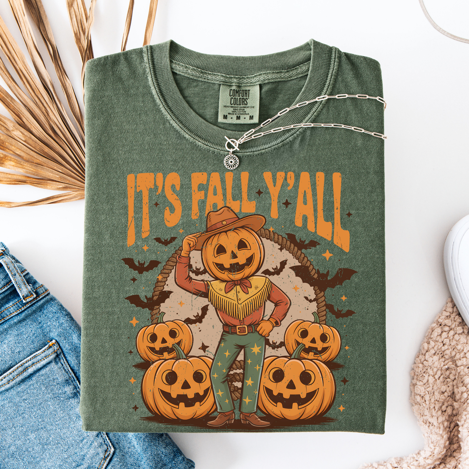 Green t-shirt with 'It's Fall Y'all' design featuring a scarecrow and pumpkins, displayed with jeans and a necklace.