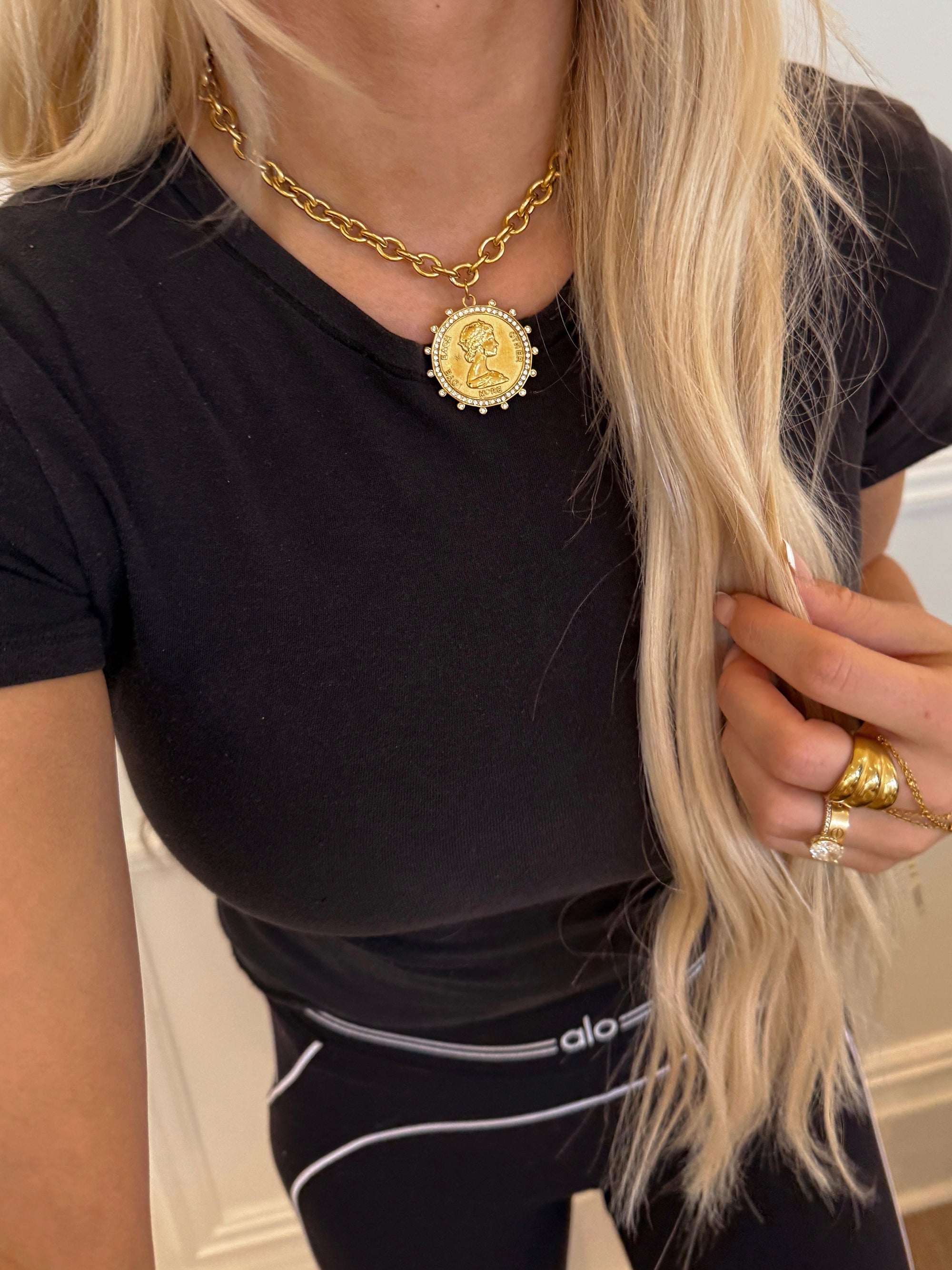 Person wearing a black t-shirt and gold necklace with a coin pendant.