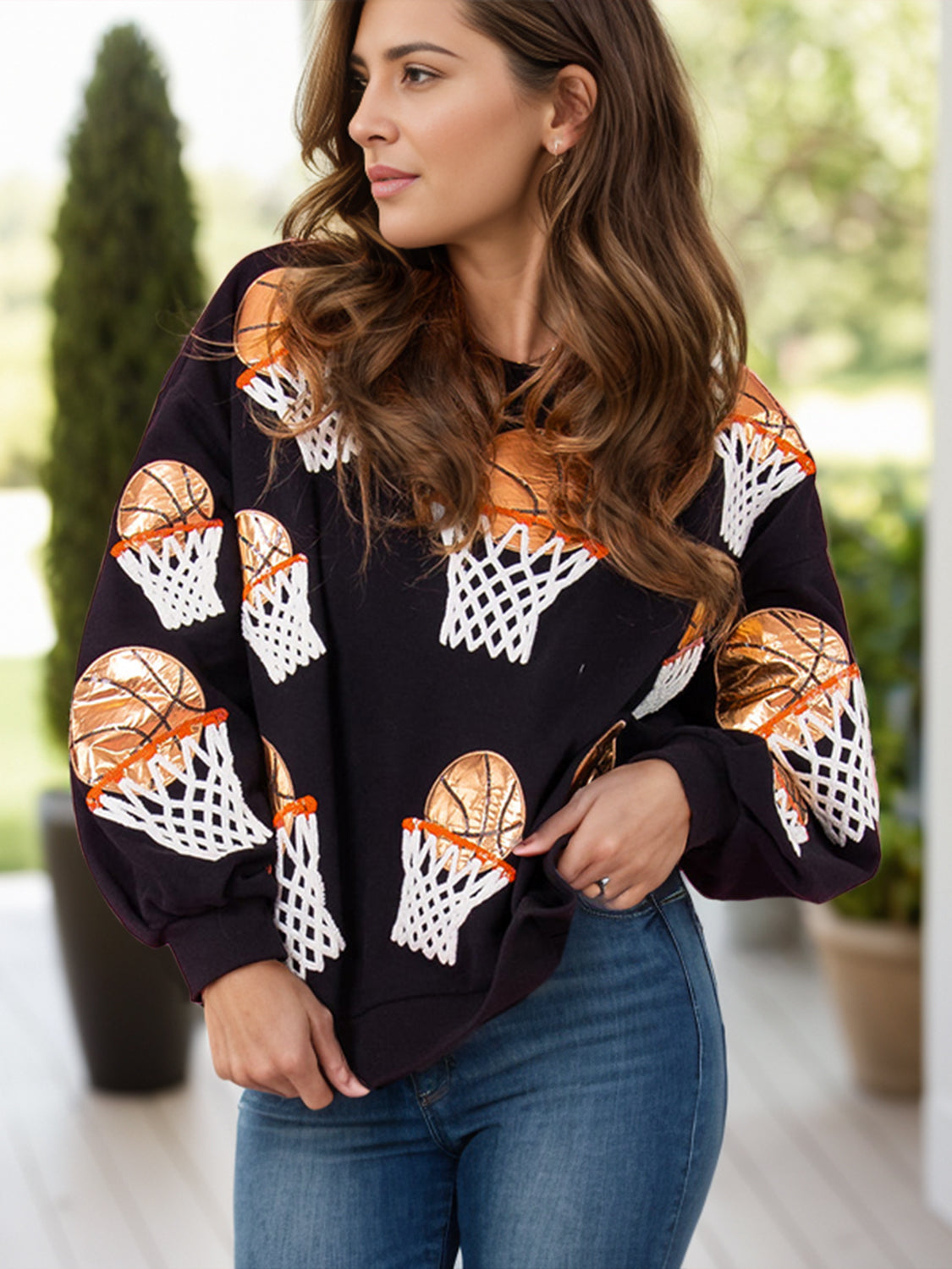 A woman wearing a round neck long sleeve sweatshirt with basketball hoop prints, paired with jeans.
