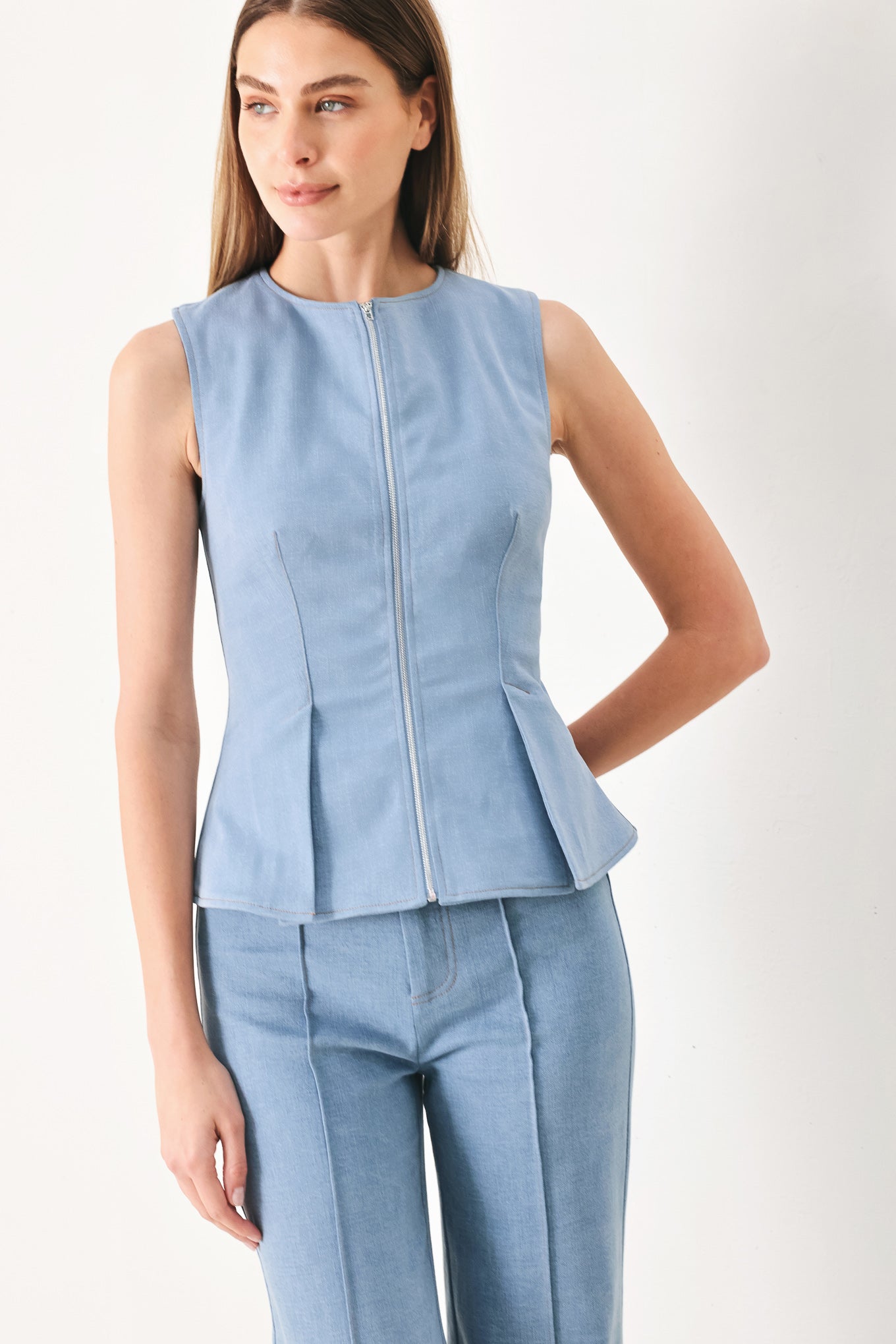 Woman wearing a light blue sleeveless peplum top and pants on a white background