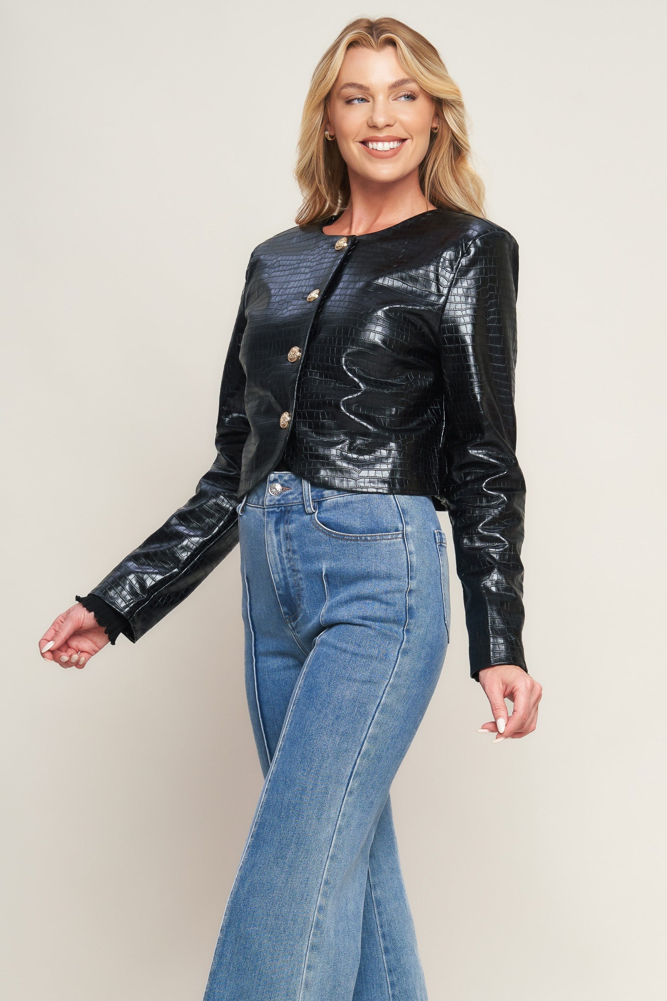 Woman wearing a black leather jacket and blue jeans against a plain background