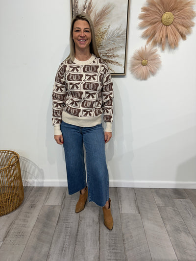 Person wearing a patterned sweater and blue jeans standing in a room with decorative elements.