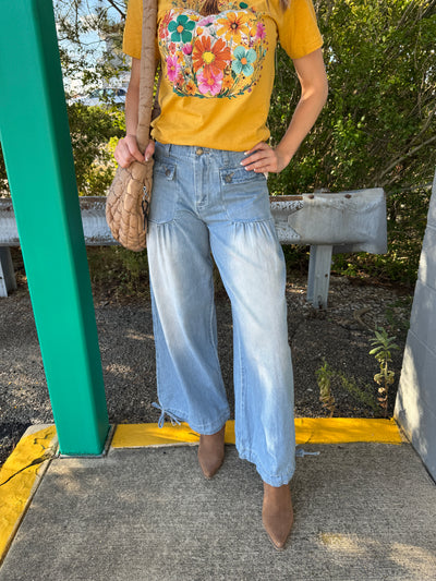 Person wearing a yellow shirt with a floral pattern, light blue jeans, and brown shoes standing on a green and yellow metal structure.