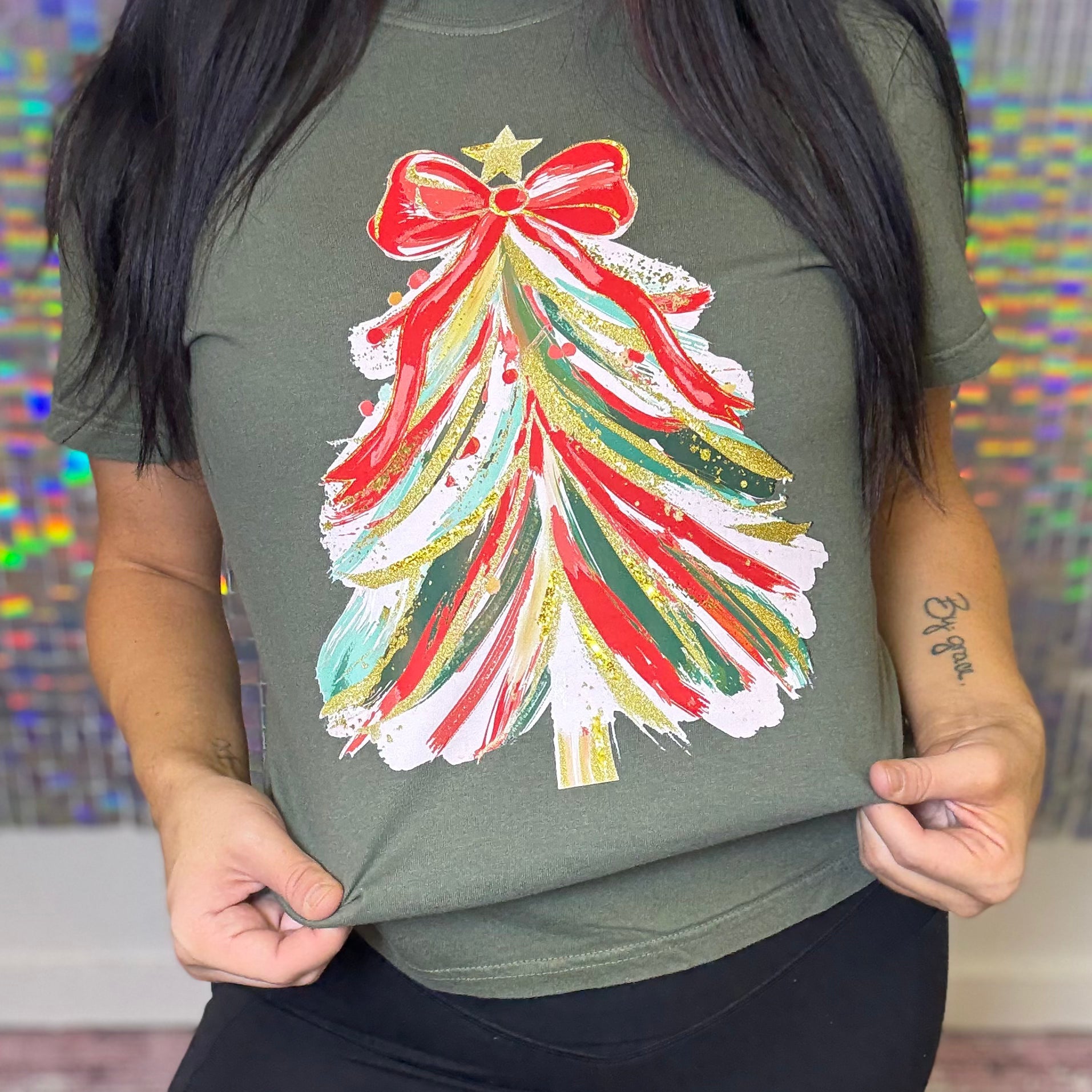 Person wearing a green t-shirt with a colorful Christmas tree design.