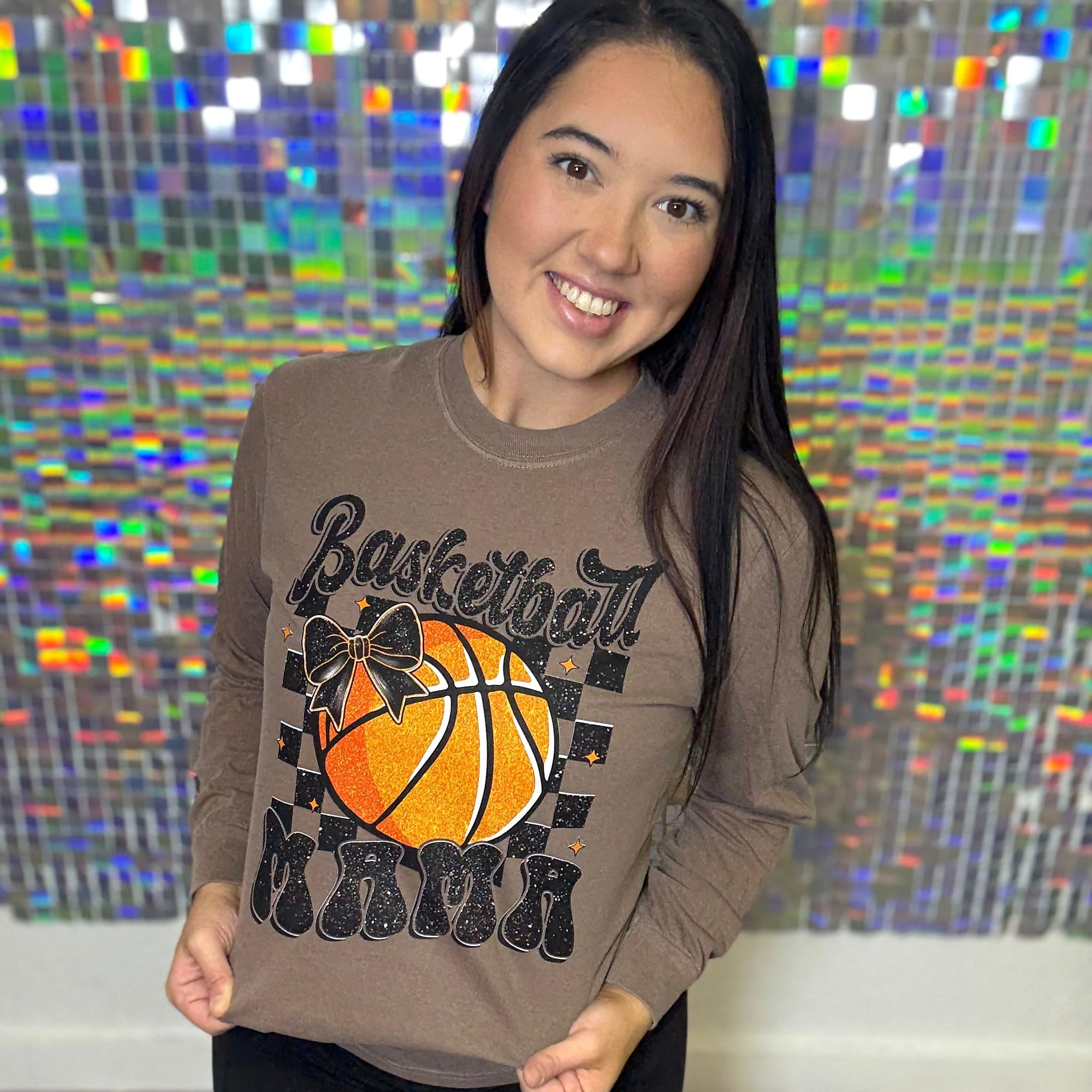 Woman wearing a brown sweatshirt with a basketball design in front of a colorful, pixelated background.