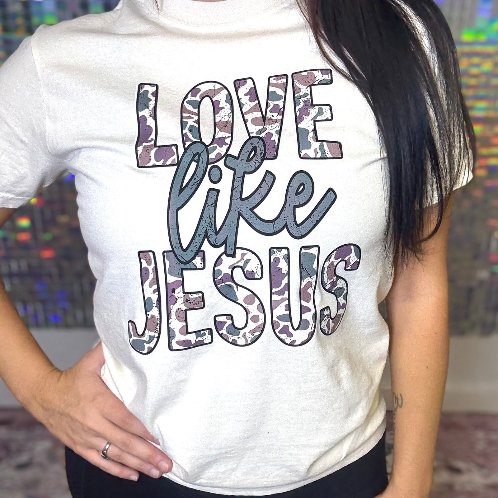 White t-shirt with 'Love like Jesus' text worn by a person, colorful background