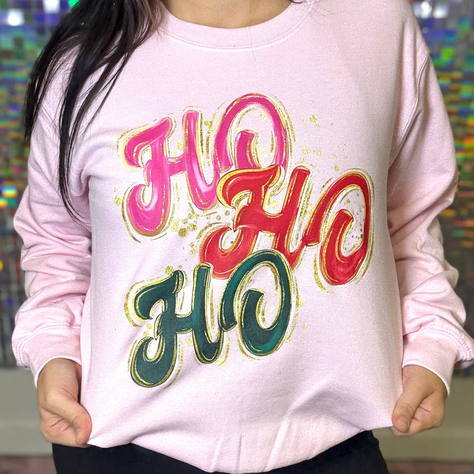 Pink sweatshirt with colorful 'Ho Ho Ho' text worn by a person, multicolored background
