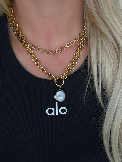 Gold chain necklace with a pendant on a person wearing an 'alo' shirt.