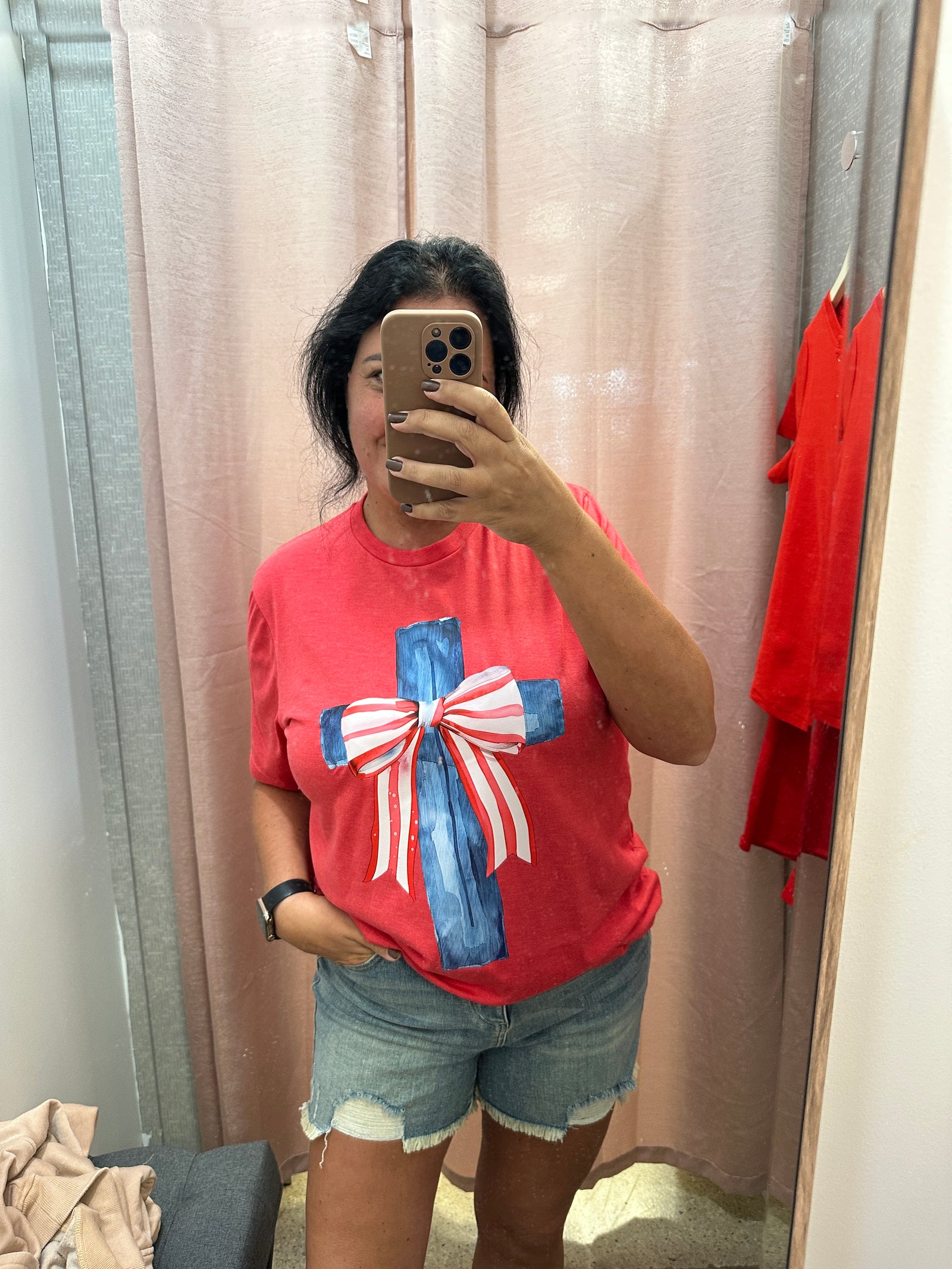 Person wearing a red shirt with a graphic design, taking a mirror selfie.