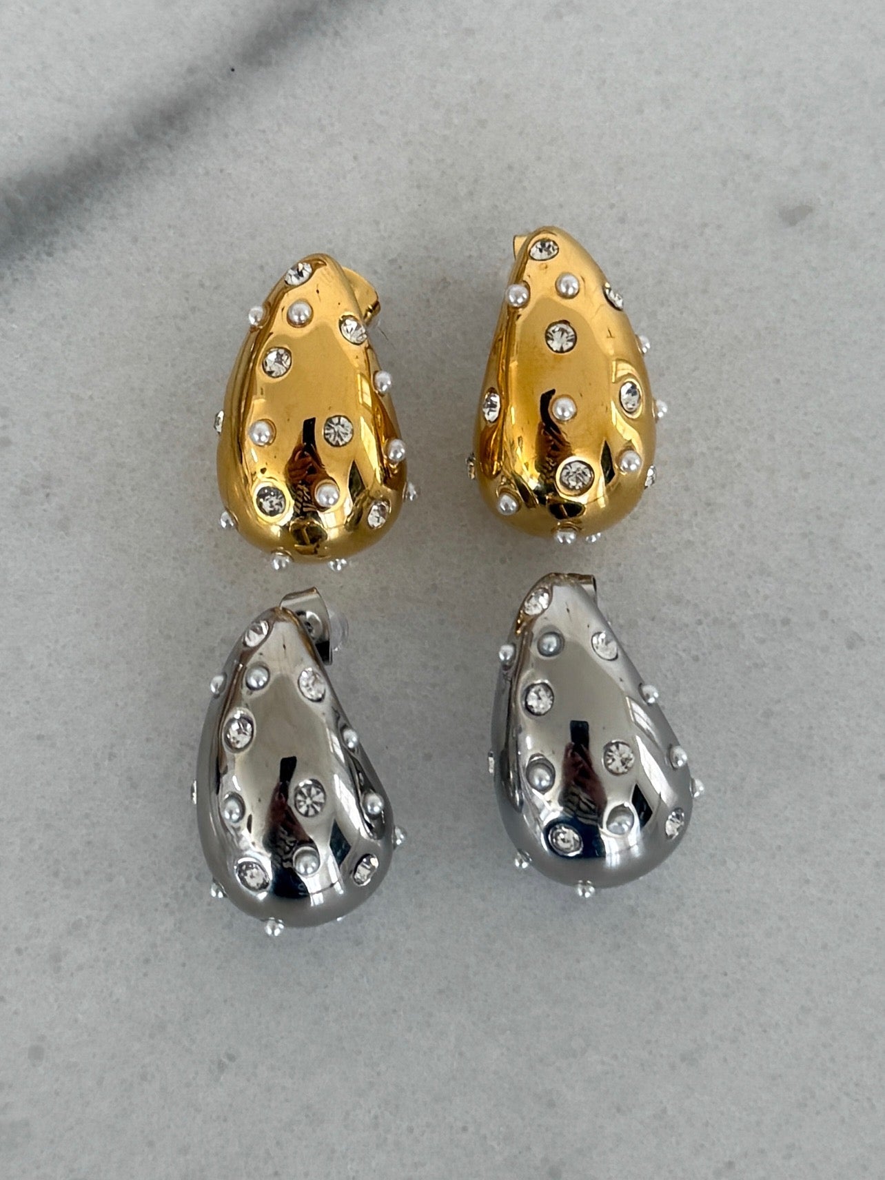Pair of gold and silver teardrop-shaped earrings on a gray background