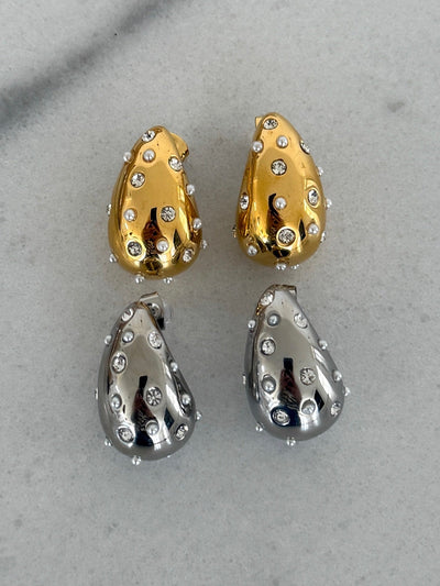 Pair of gold and silver teardrop-shaped earrings on a gray background