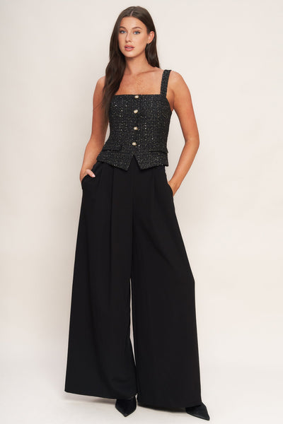 Woman wearing a black sleeveless top with buttons and wide-leg pants on a white background