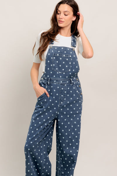 Woman wearing a blue polka dot denim jumpsuit against a plain background