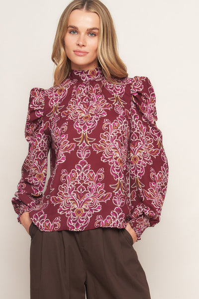 Woman wearing a burgundy patterned blouse with brown pants on a white background