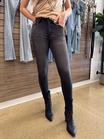 Person wearing black jeans and black boots standing on a wooden floor with folded jeans and pants in the foreground.