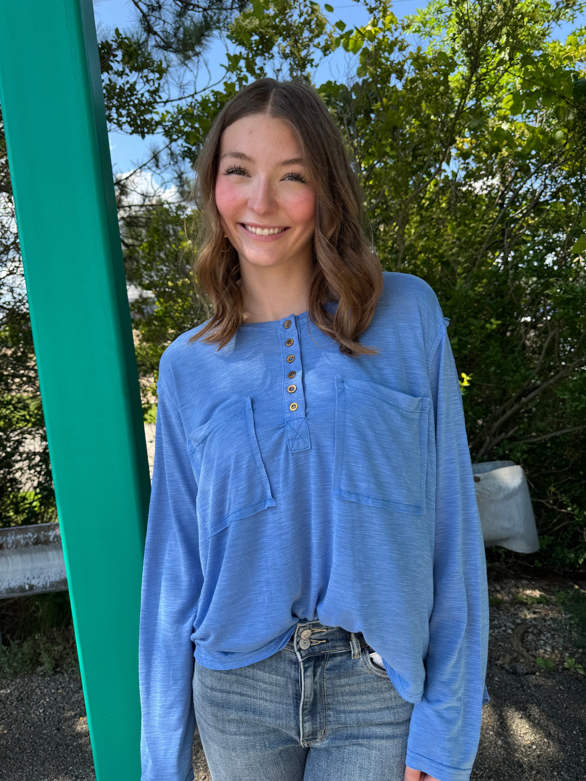 Person wearing a blue shirt standing outdoors with trees in the background