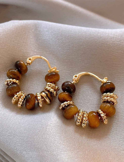 Pair of hoop earrings with brown beads and gold accents on a light fabric background