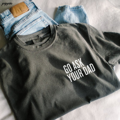 Black sweatshirt with 'GO ASK YOUR DAD' text on a light gray surface with jeans in the background.
